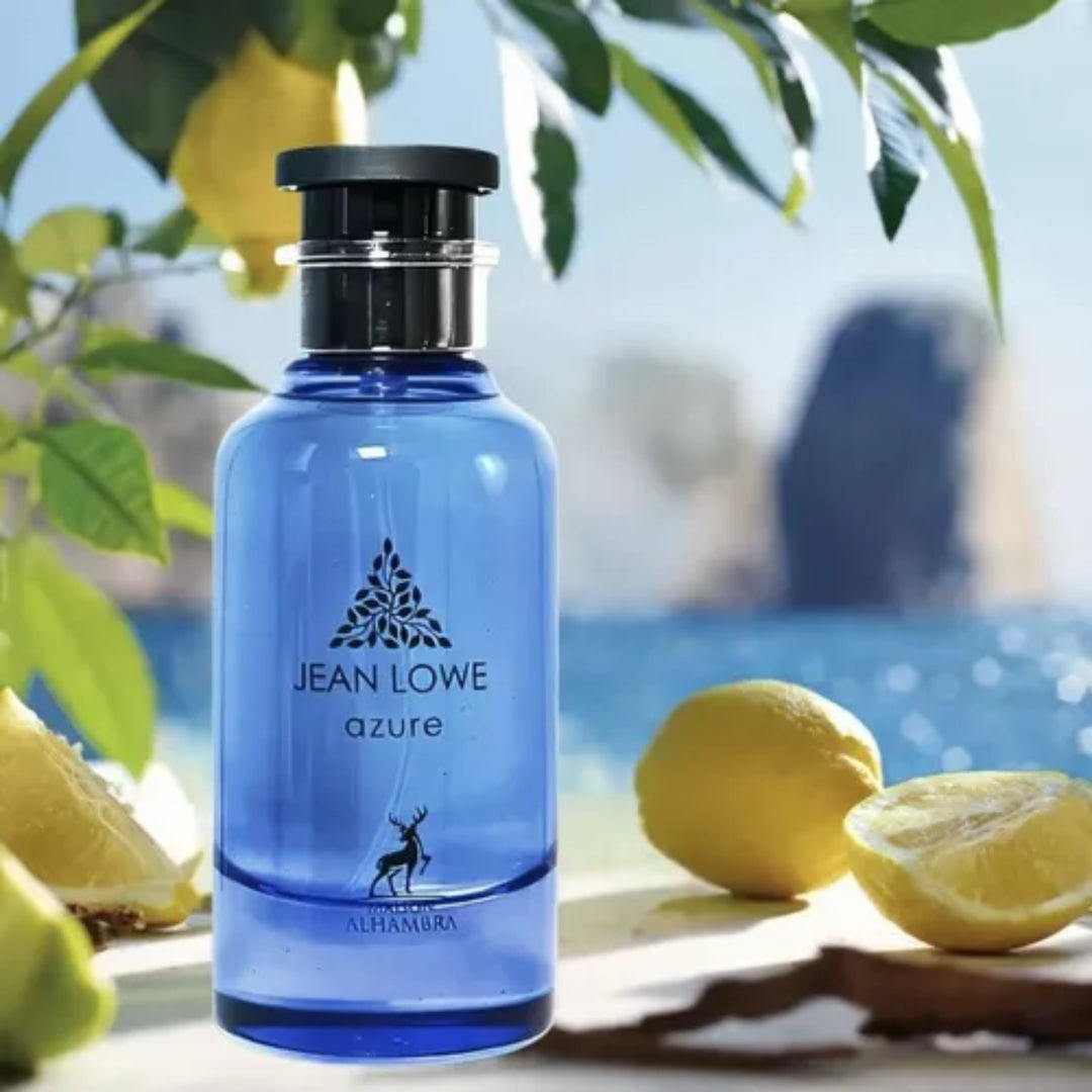 Botella de perfume Jean Lowe Azure de Maison Alhambra sobre fondo veraniego con limones y mar mediterráneo.
